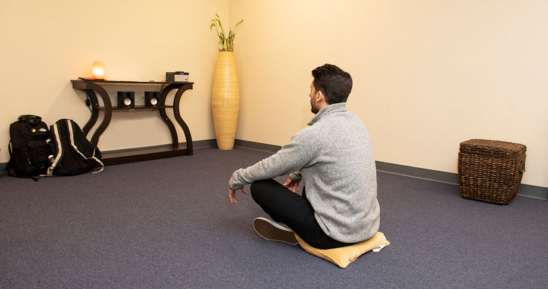 Student meditating on a pillow on the floor in the meditation room at PCOM's Philadelphia campus