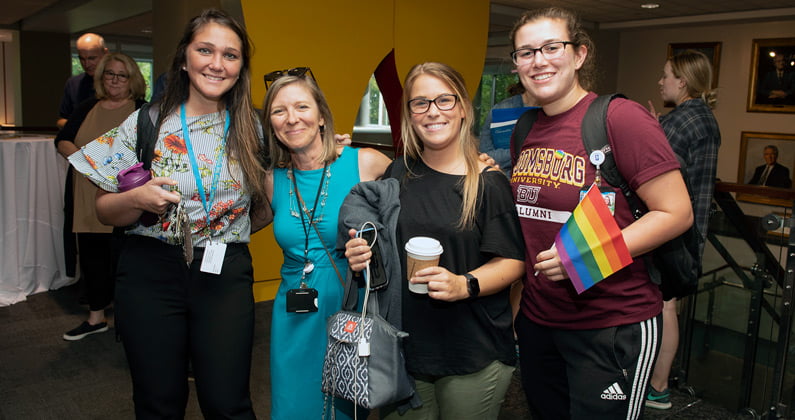 Group of four female students and faculty smile while holding pride flags at the 2019 LGBTQIA Welcome Reception event