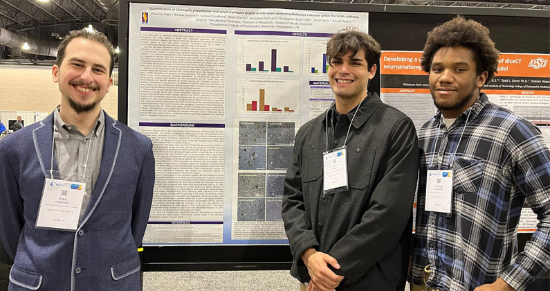 PCOM research interns smile in front of their research poster at a conference in 2022