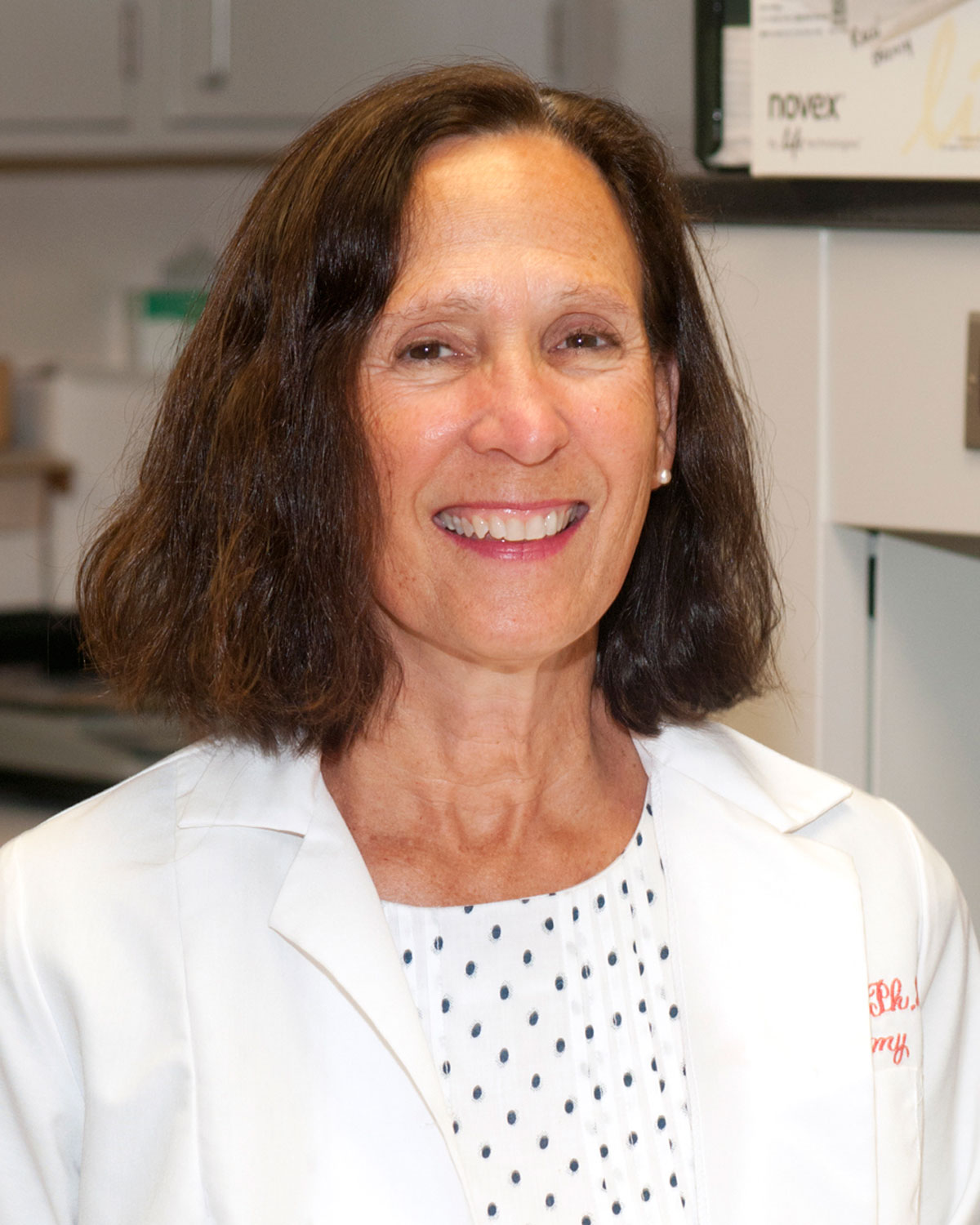 Mindy George-Weinstein, PhD, smiling in her white lab coat in a PCOM laboratory