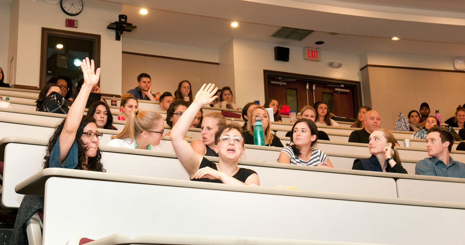 Med and grad students raise their hands during a lecture in a PCOM lecture hall