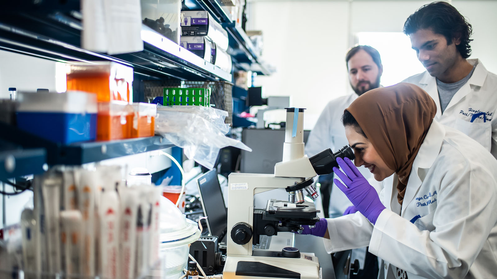 A biomedical sciences student peers into a microscope in a lab at PCOM