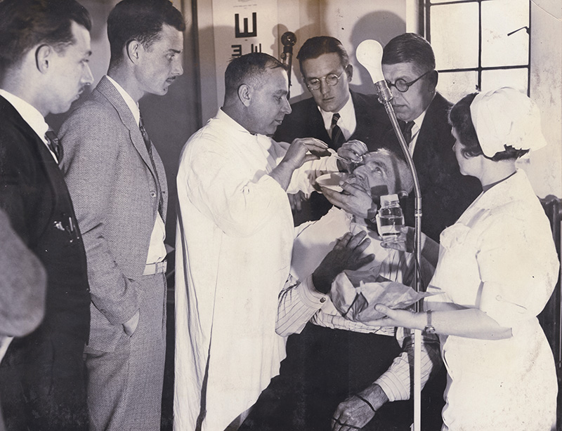 Medical students observe a faculty member giving treatment to a patient (1950s).