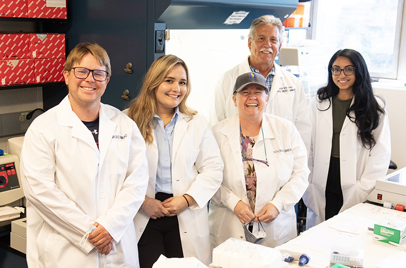 Dr. Balin along with research students and staff smile in a laboratory, 2023.