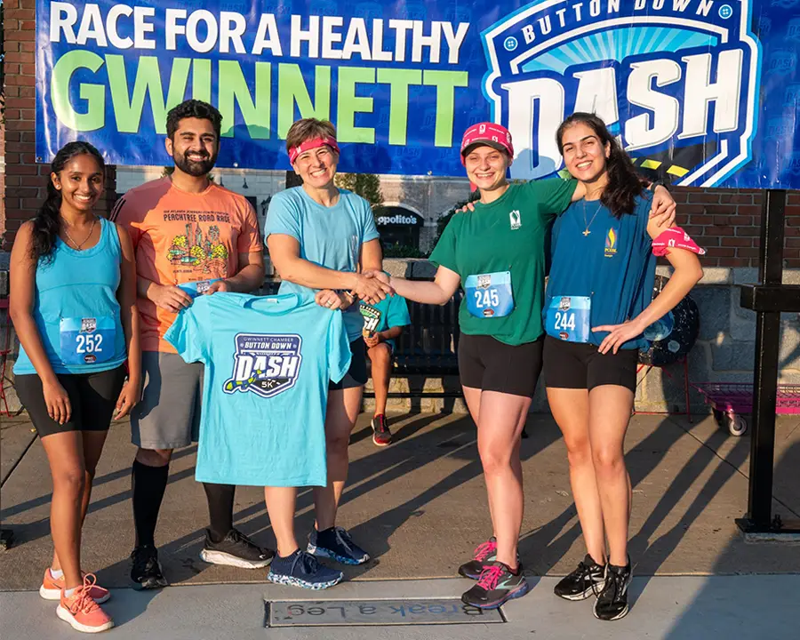 PCOM Georgia's Dean Mann smiles with students in front of a 5K sign in Gwinnett County, GA