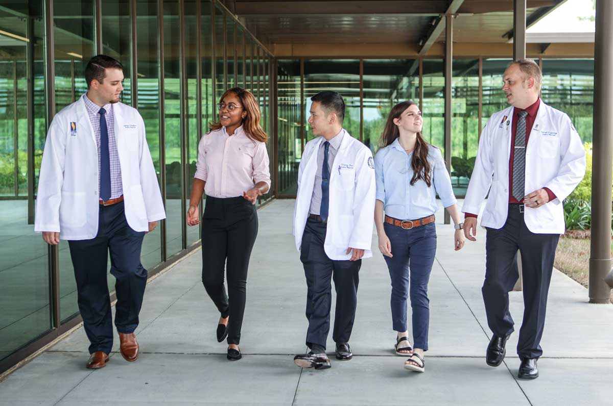 A group of students walks together on a sidewalk under an awning at PCOM South Georgia.