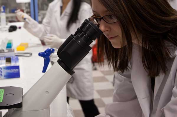 A female medical laboratory scientist looks into a microscope.