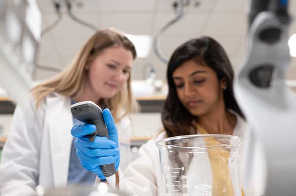 Two female medical laboratory scientists in white coats are shown working with laboratory equipment.