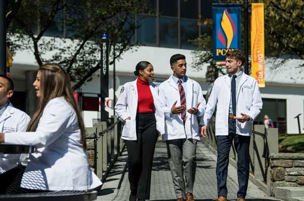 Three PCOM medical students in white coats walk towards the Philadelphia campus central courtyard.