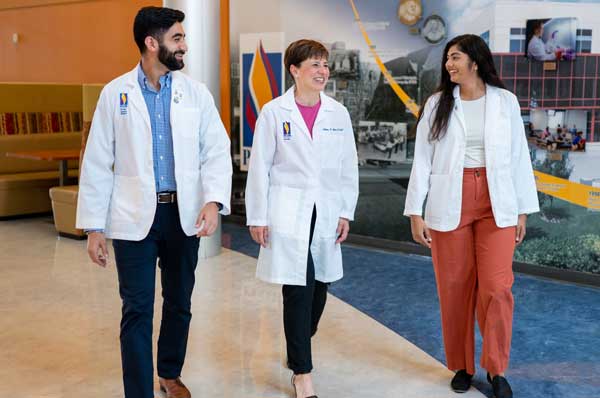 A female professor walking down the hall with a male medical student and a female medical student.