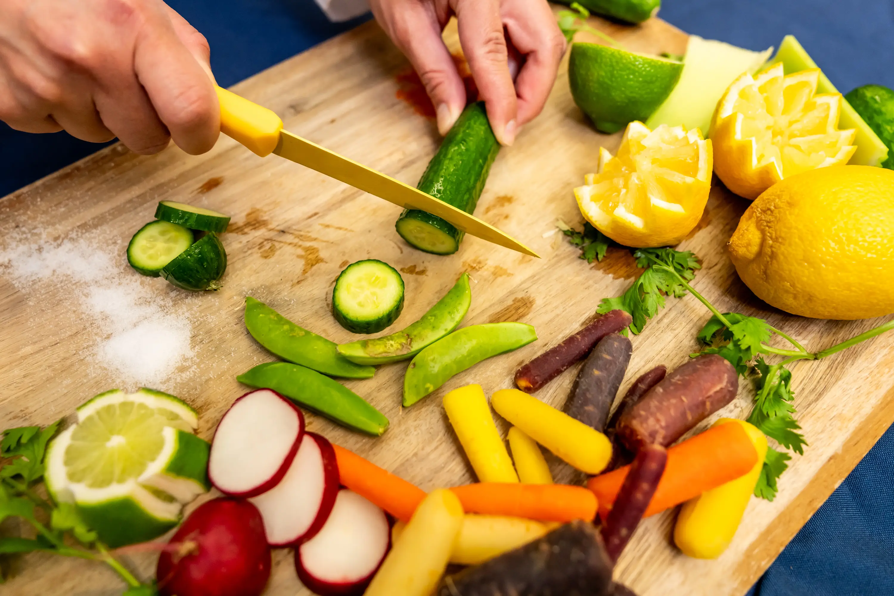 A student cuts zucchini on a cutting board filled with fruits and vegetables.
