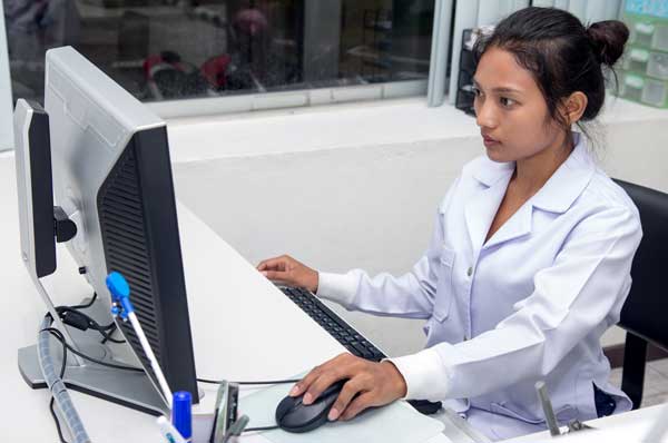 A female informatics pharmacist in a white coat works at a computer.