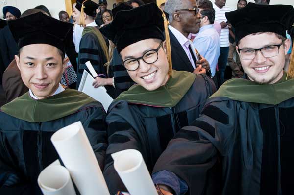 Three Doctor of Pharmacy students in regalia are shown at a commencement ceremony.