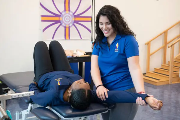A smiling DPT student practices therapy with another student