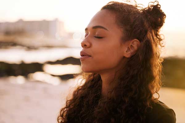 A young woman with her eyes closed and a serene look on her face tilts her head upward.