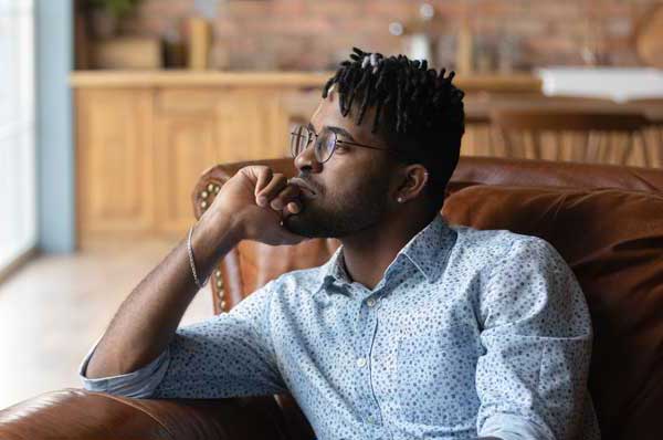 A Black male sits in a chair and looks lost in thought.