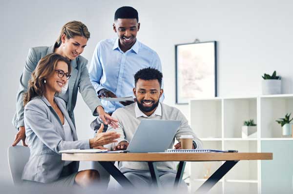 A group of smiling people look at a laptop computer screen together.