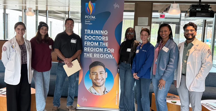 PCOM students and staff pose around marketing banner