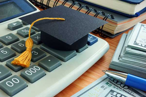 A graduation cap on a calculator surrounded by money.