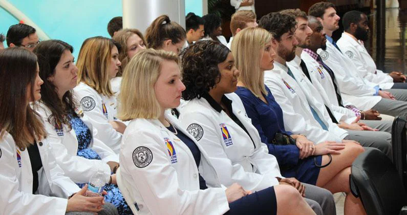 Seated PCOM Georgia students in white coats face the front of the room. 