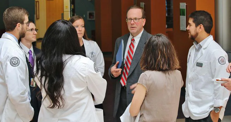 Jeffrey K. Seiple and PCOM Georgia students wearing white coats stand in a circle together.
