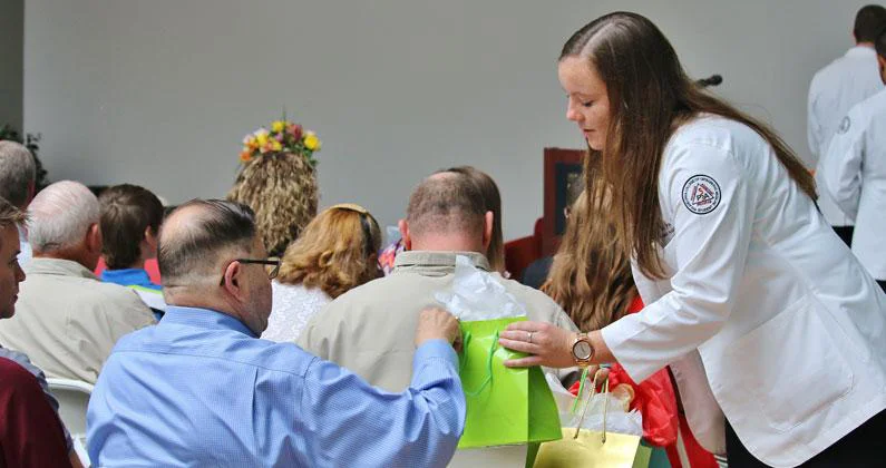 A PCOM Georgia student hands a green gift bag to a seated guest.