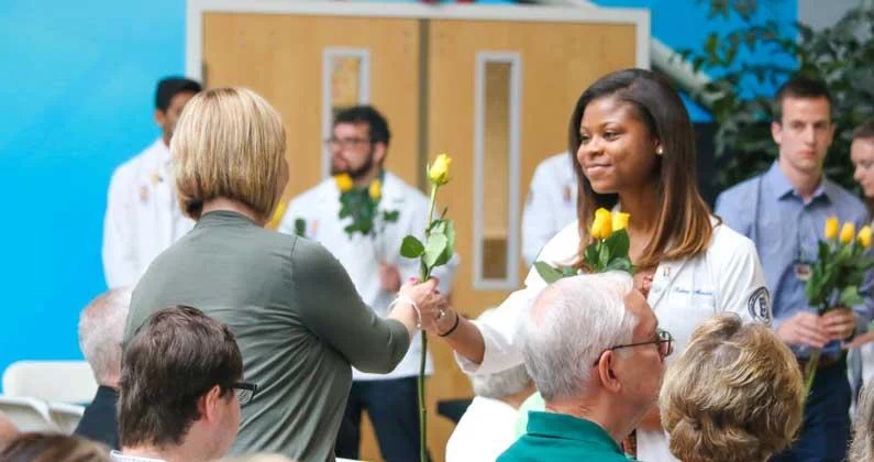 A medical student in a white lab coat hands a yellow rose to a audience member