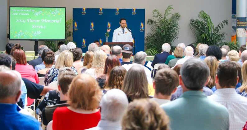 A medical student in a white lab coat addresses the audience while standing at a podium