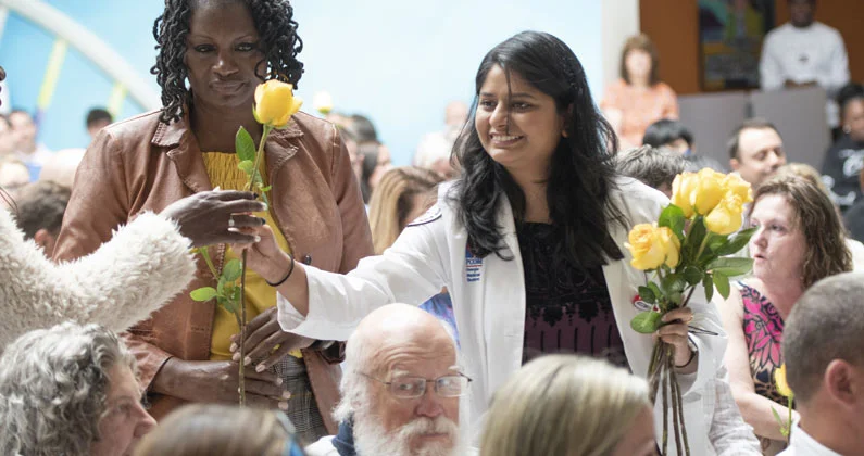 A medical student hands yellow roses to attendees