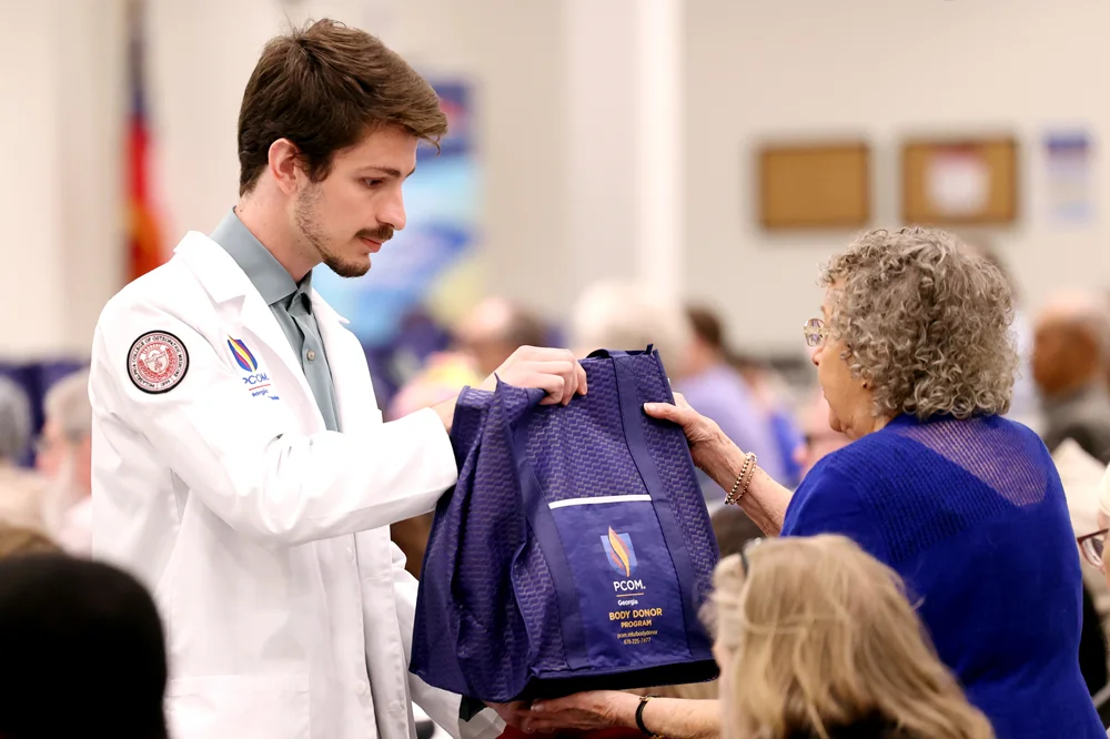 A DO student hands a bag to an attendee