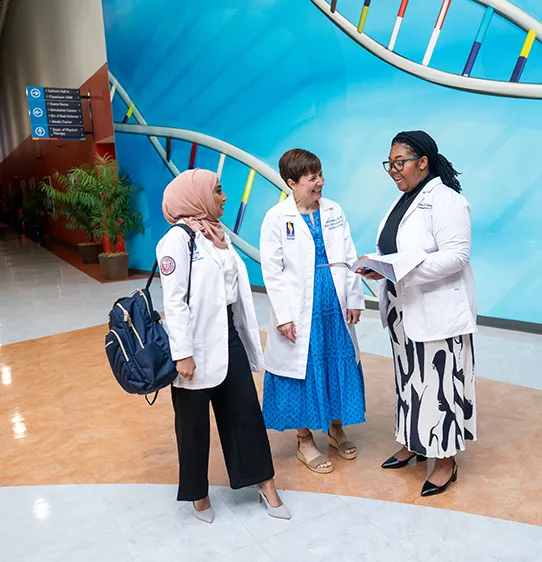 Medical students and DO faculty looking at a textbook in a hallway at PCOM Georgia