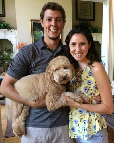 Eric Eck, MS/PA '19, smiles in his home with his fiancee and golden doodle, Murph