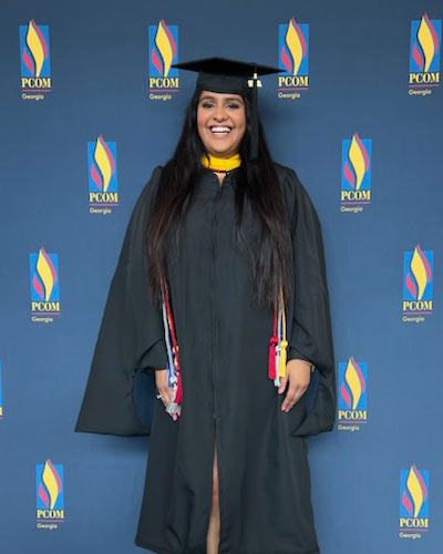 Avini Sharma, MS,  wears her cap and gown and smiles at PCOM Georgia's biomed graduation