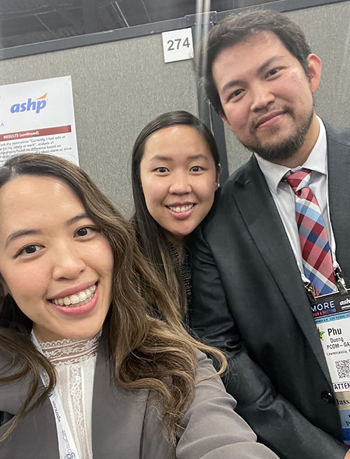 Three PCOM pharmacy students take a selfie wearing suits at a research poster presentation event.