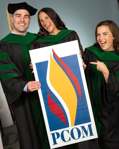 Katie O'Shea and friends hold a PCOM sign on graduation day