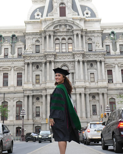 Katie O'Shea, DO ’23 poses in commencement regalia on the streets of Philly