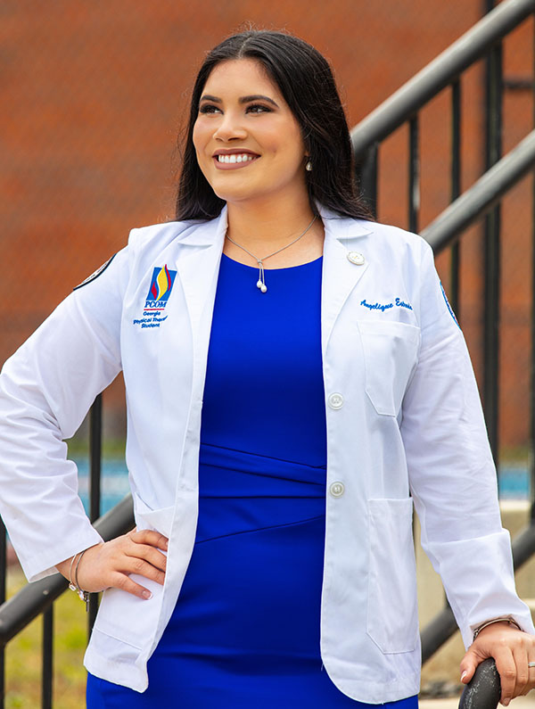 DPT graduate Zelma Angelique Estrada-Womack standing outside in her white coat smiling