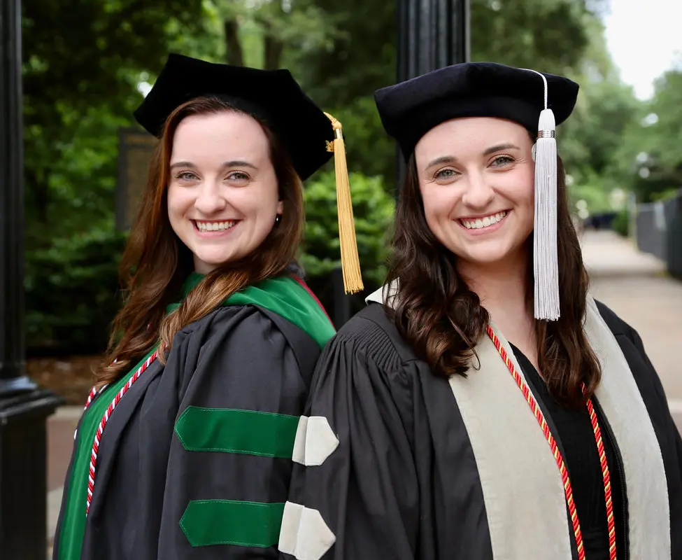 Macy Rowan, DO '24, and her twin sister Morgan Rowan smile in their med school caps and gowns