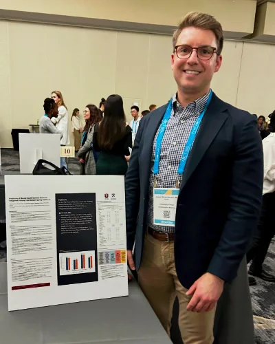 Joseph Harrison, PsyD ‘25, poses for photo standing next to research poster