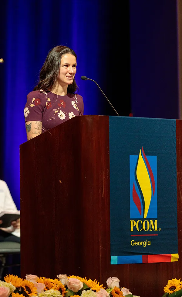 PCOM graduate Madison Cohen, DO '25, smiling and speaking at a podium during an event
