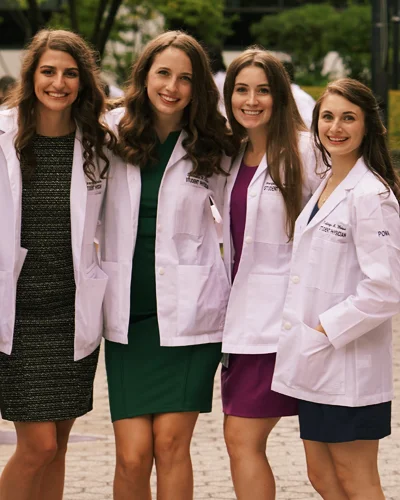 Samantha Cooper and fellow DO graduates stand together wearing white coats