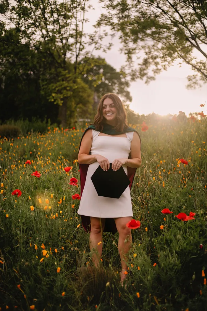 PCOM Georgia DPT graduate Sarah Grady smiling in a field of white flowers wearing a white dress along with her graduation garb
