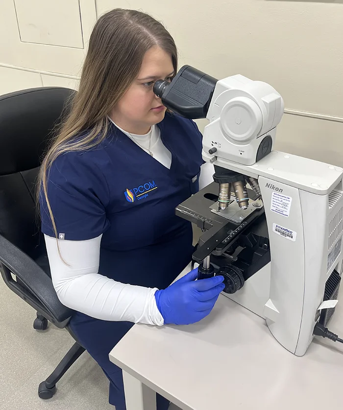 PCOM Georgia MLS grad Leslie Walden smiles as she looks through a microscope in a laboratory