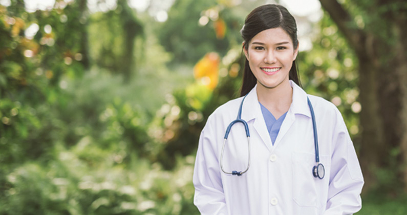 Student doctor smiling wearing her physician white coat in front of a Georgia summer landscape