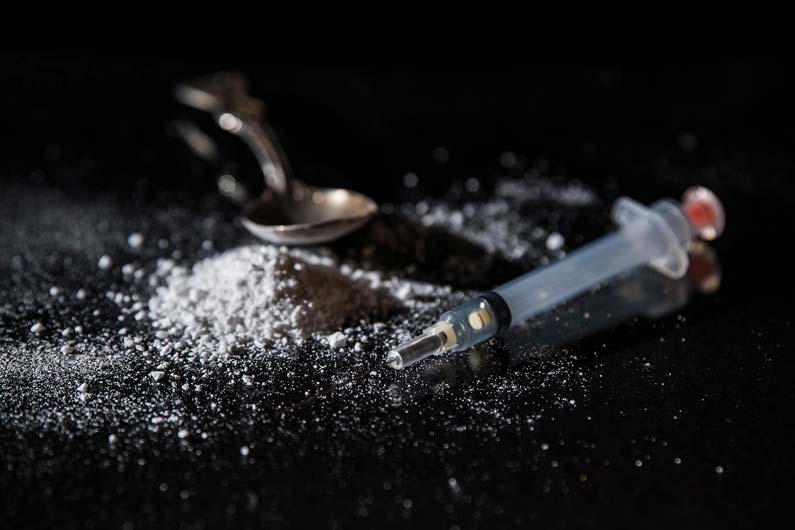 Photograph of heroine, syringe and spoon on a table.