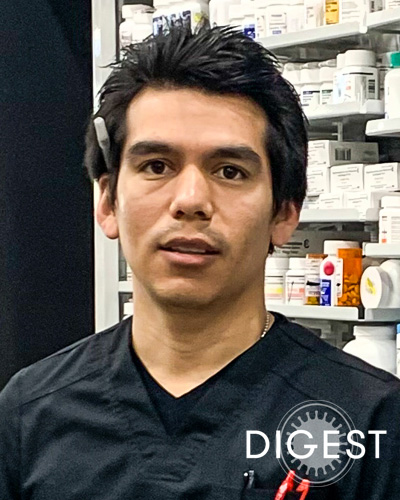 James Nick Hernandez, PharmD ’19, looks at the camera wearing scrubs in a pharmacy.