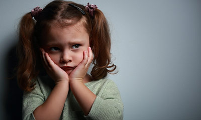 Small girl holds her face and frowns while stressed