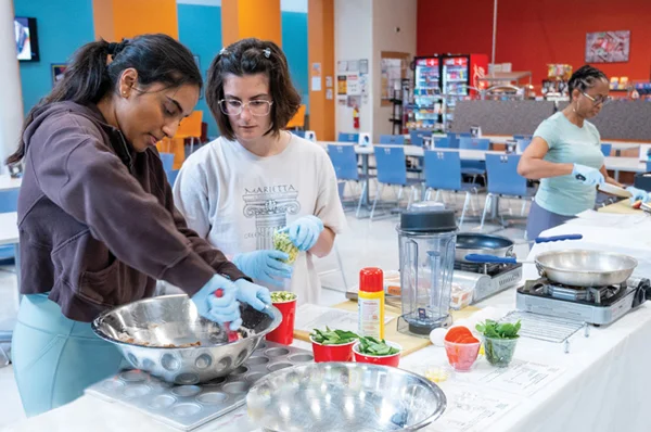 Two students mix ingredients in a stainless steel bowl