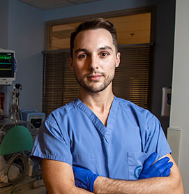 Photograph of Dustin Flannery, DO ’11 working in his blue scrubs in the neonatal intensive care unit (NICU)