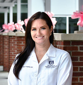 Alicia Huff Vinyard, DO '11, smiling in her white coat in front of a medical facility.